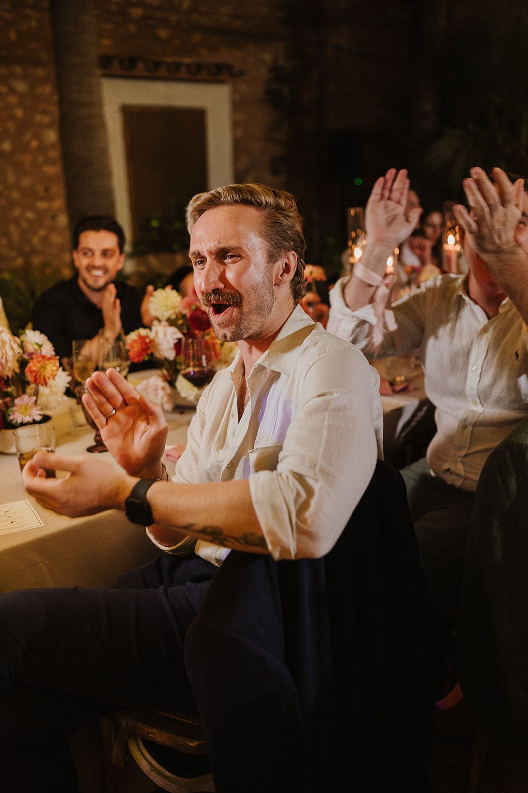 Guest claps enthusiastically at candlelit wedding reception dinner inside stone venue.
