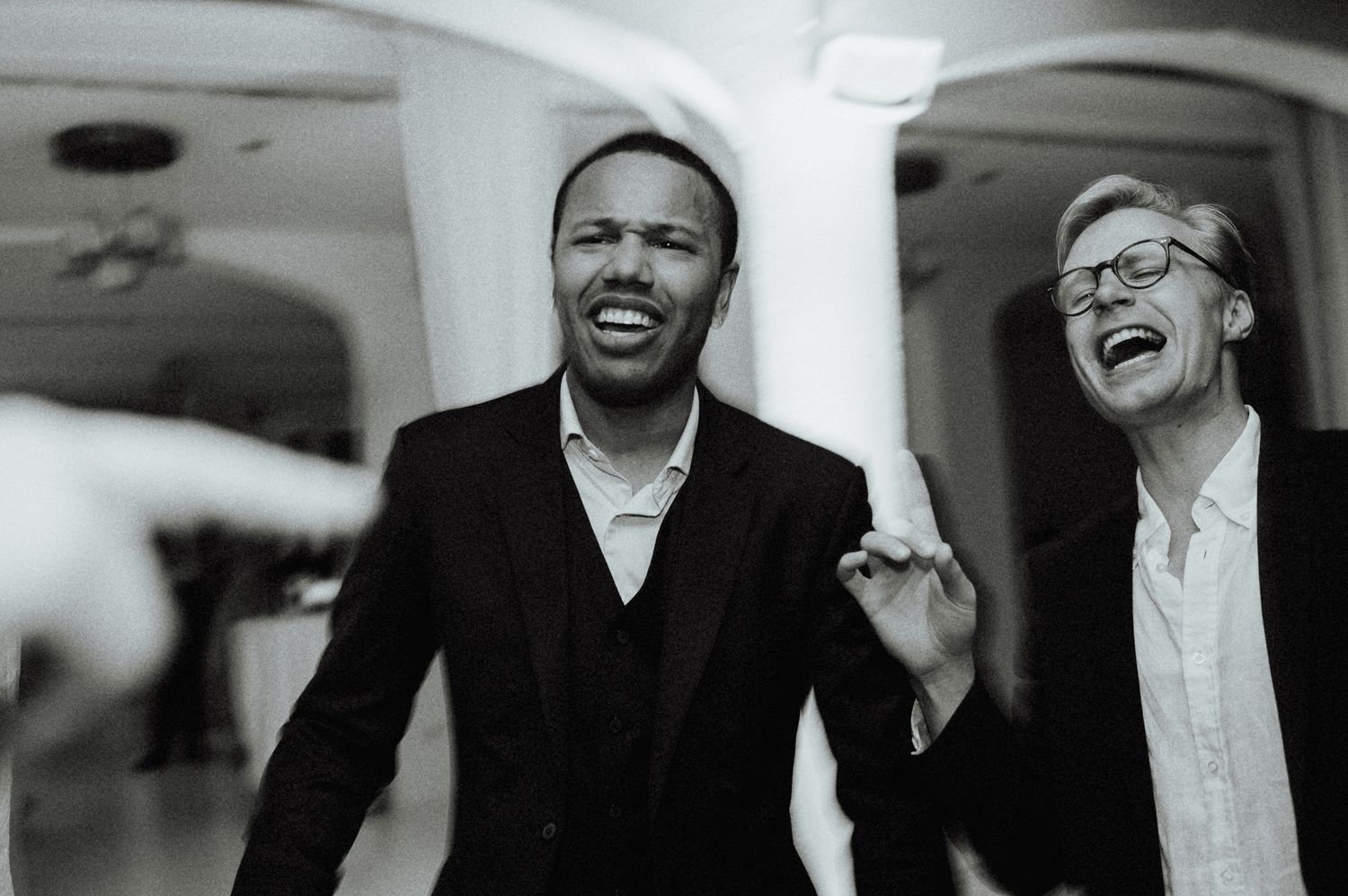 Two joyful men in suits laugh together in a candid black and white wedding reception photo.