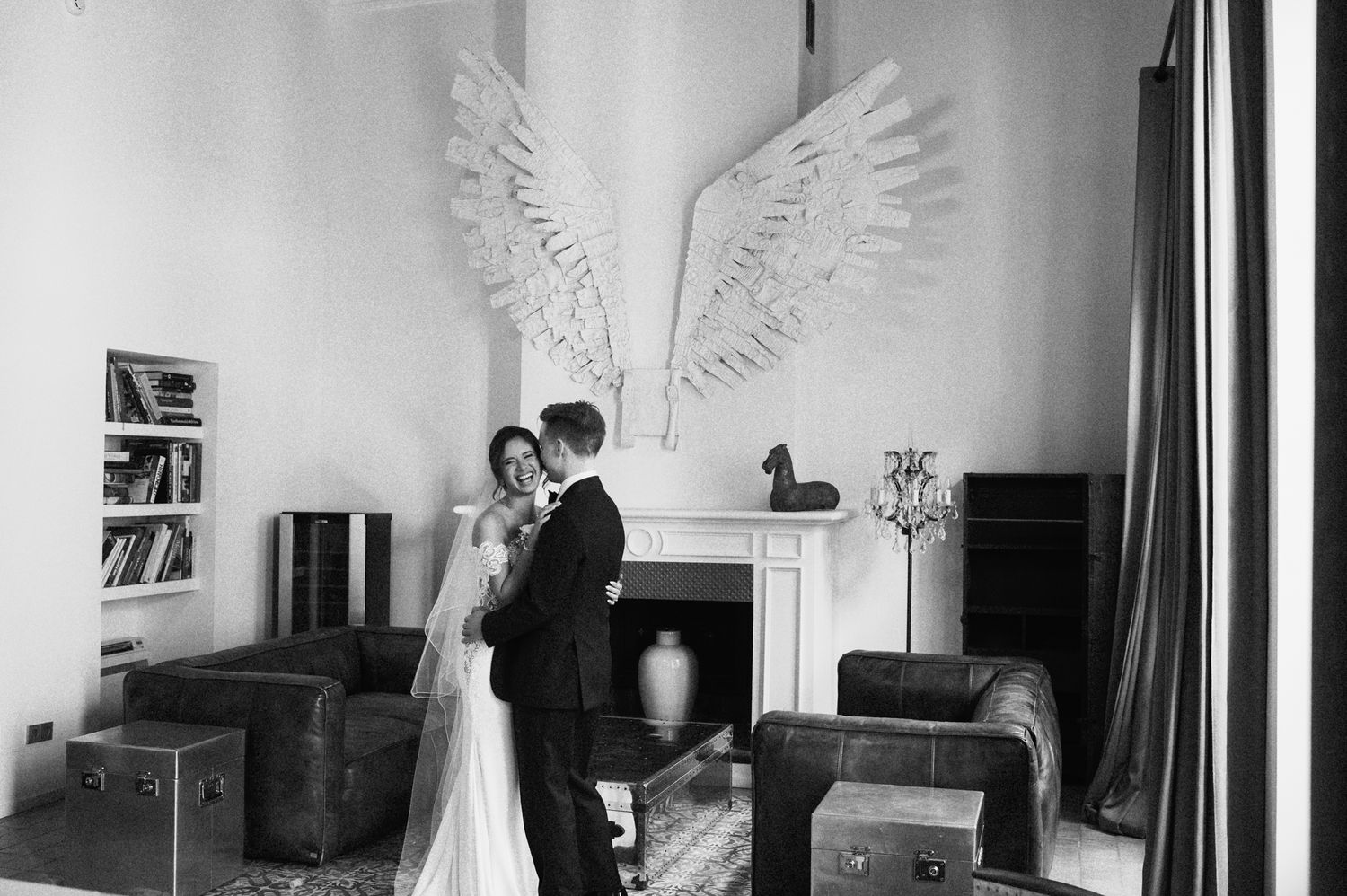 Bride and groom share romantic moment in black and white photo with large angel wings wall art.