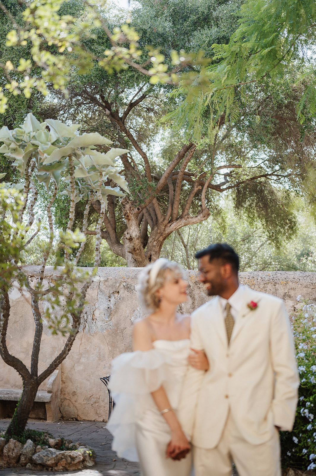 Bride and groom sharing romantic moment in lush Mediterranean garden after outdoor wedding ceremony.