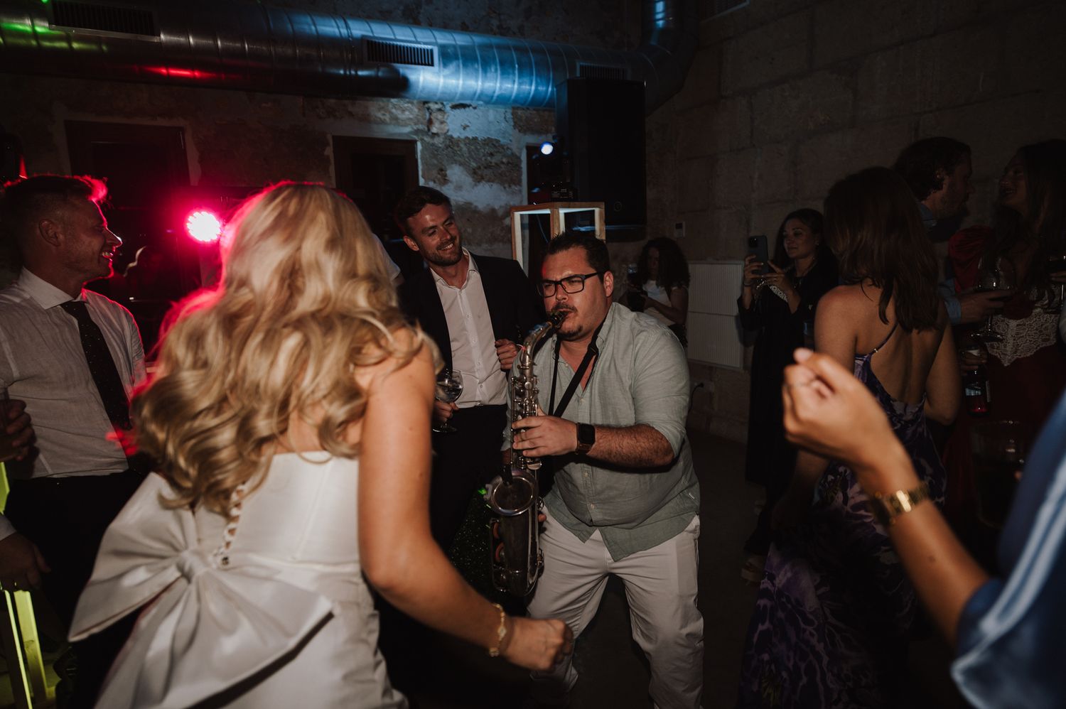 Live saxophonist in white suit performs on dance floor surrounded by guests at energetic wedding after-party.