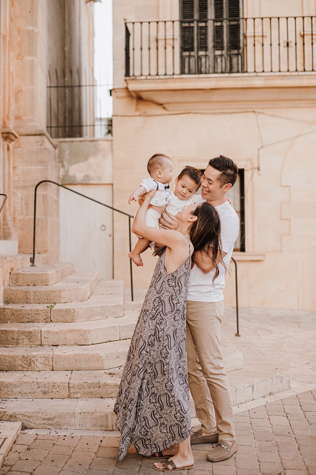 A happy family with two young children share a loving moment on sun-drenched European stone steps.