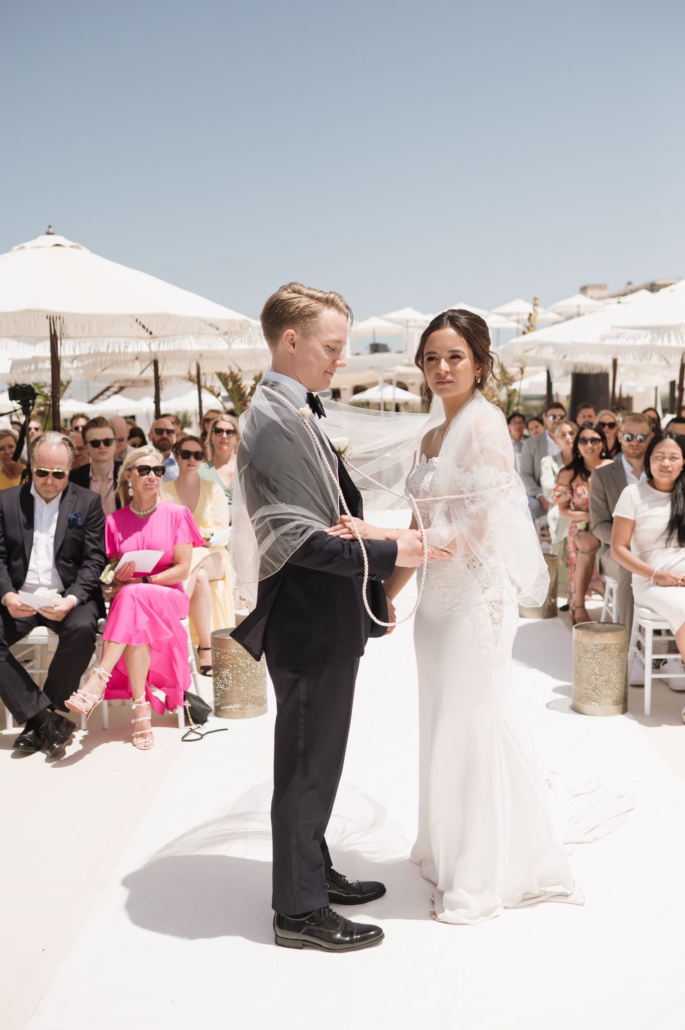 Bride and groom exchange vows at outdoor beach wedding ceremony with white umbrellas.
