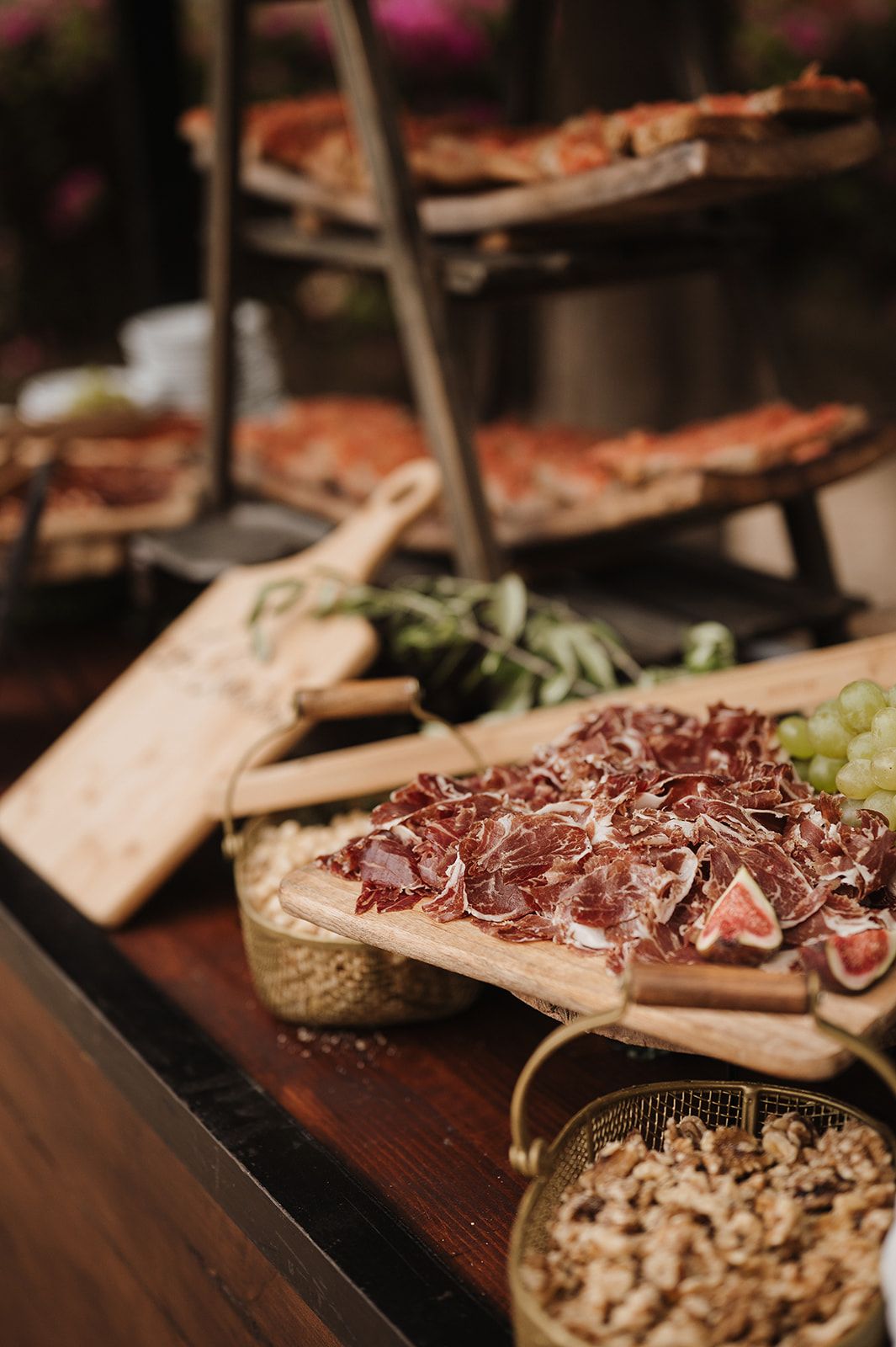 Rustic wedding charcuterie board with prosciutto, figs, grapes, and assorted appetizers on wooden serving boards.