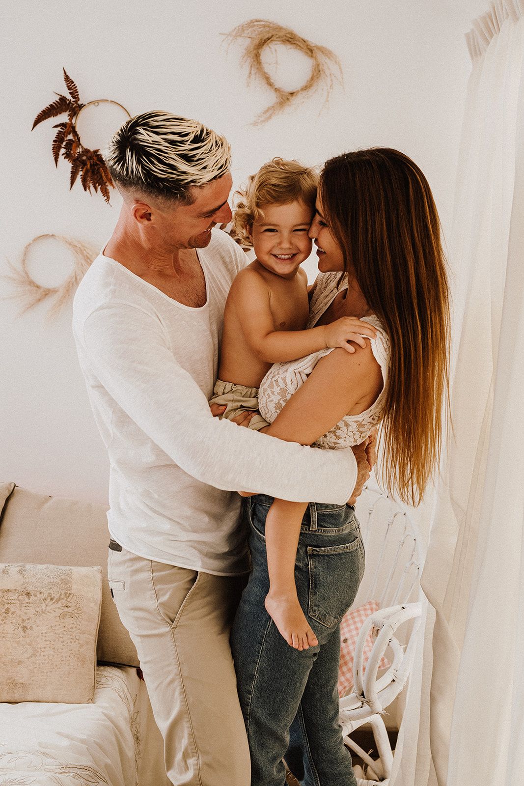 A loving family of three shares a joyful embrace, with parents kissing their smiling toddler in a bright room.