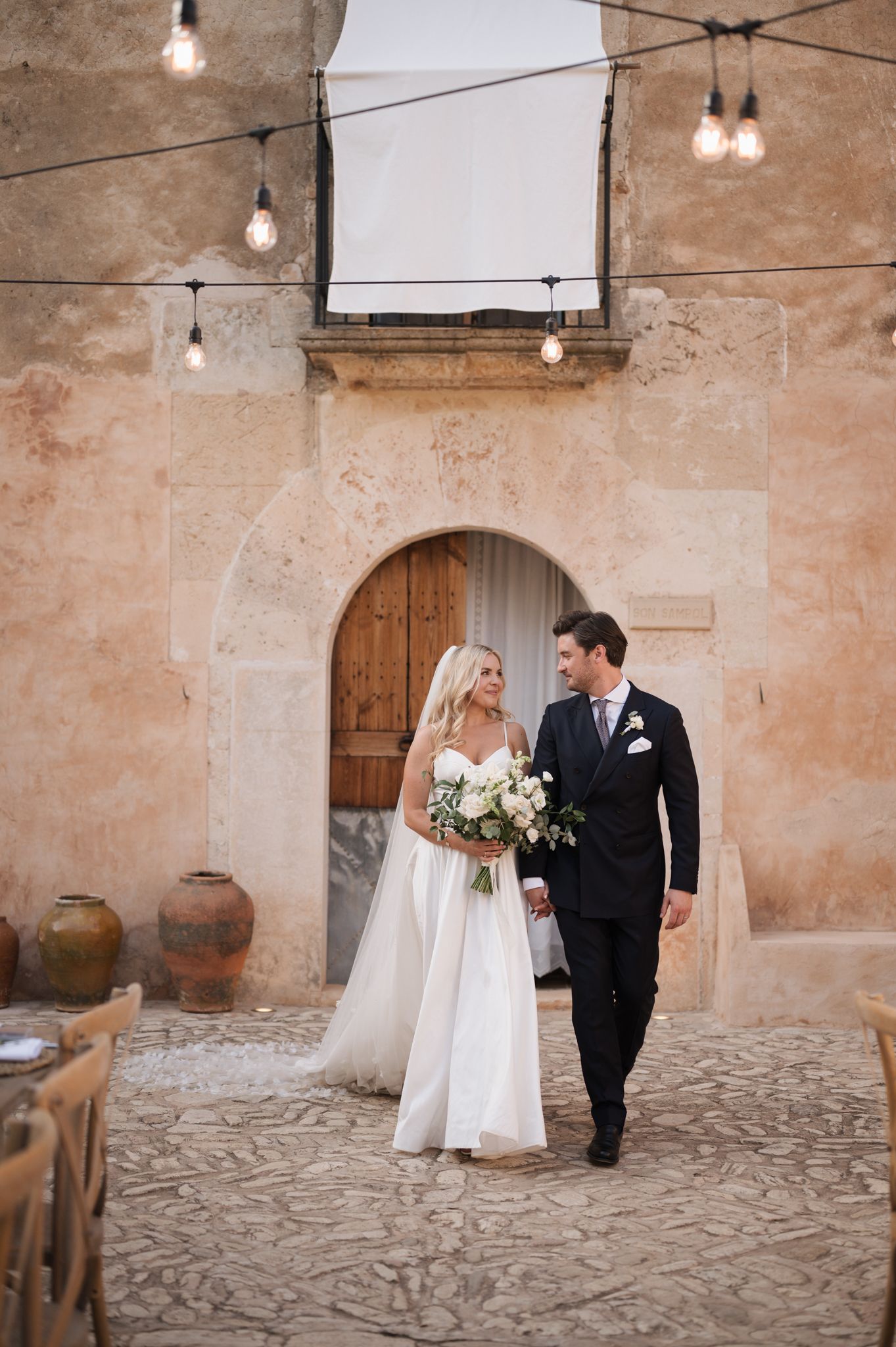 Bride and groom walking hand in hand at rustic Mediterranean wedding venue.