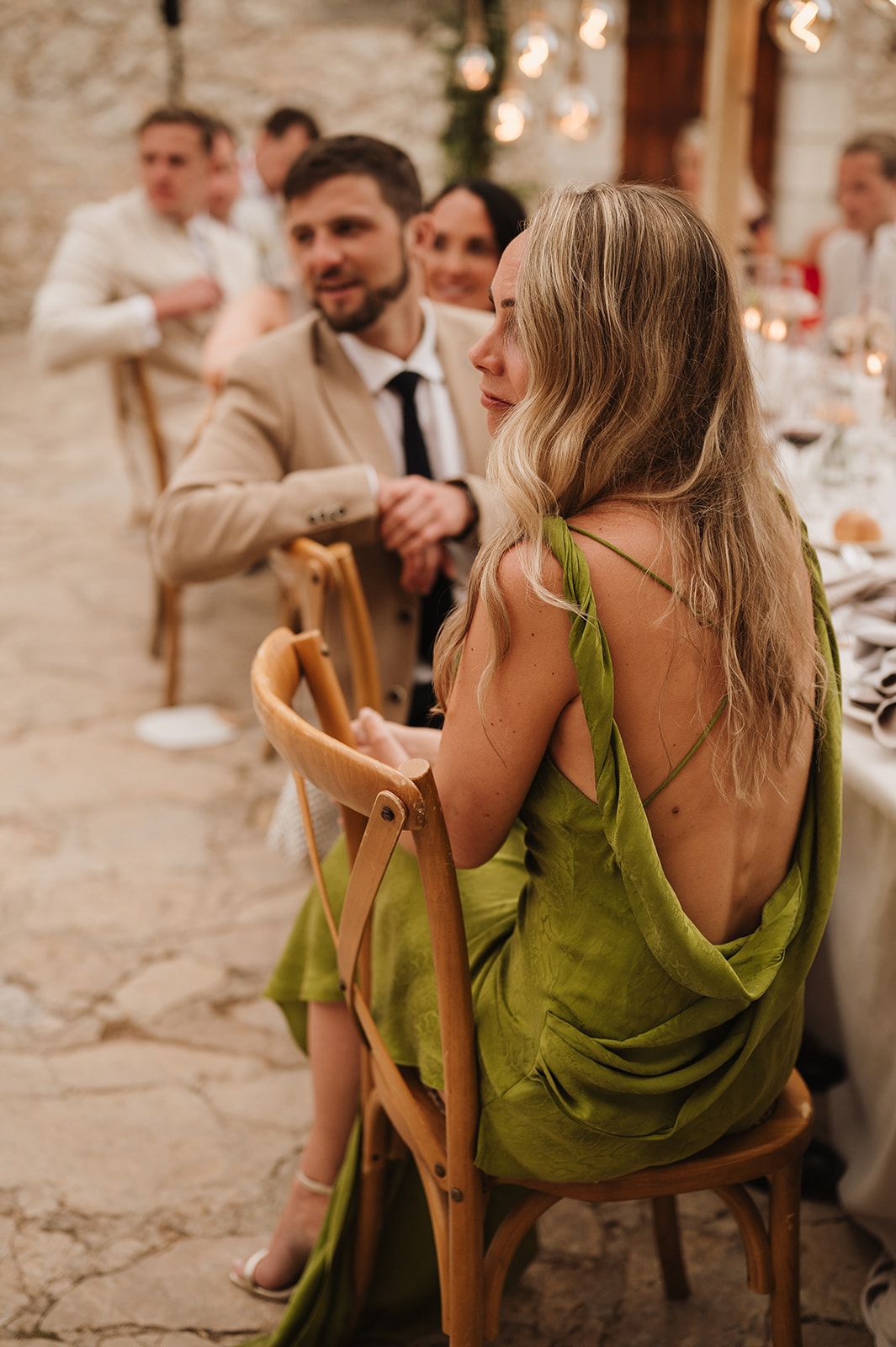 Woman in backless green dress seated at outdoor wedding reception dinner table.