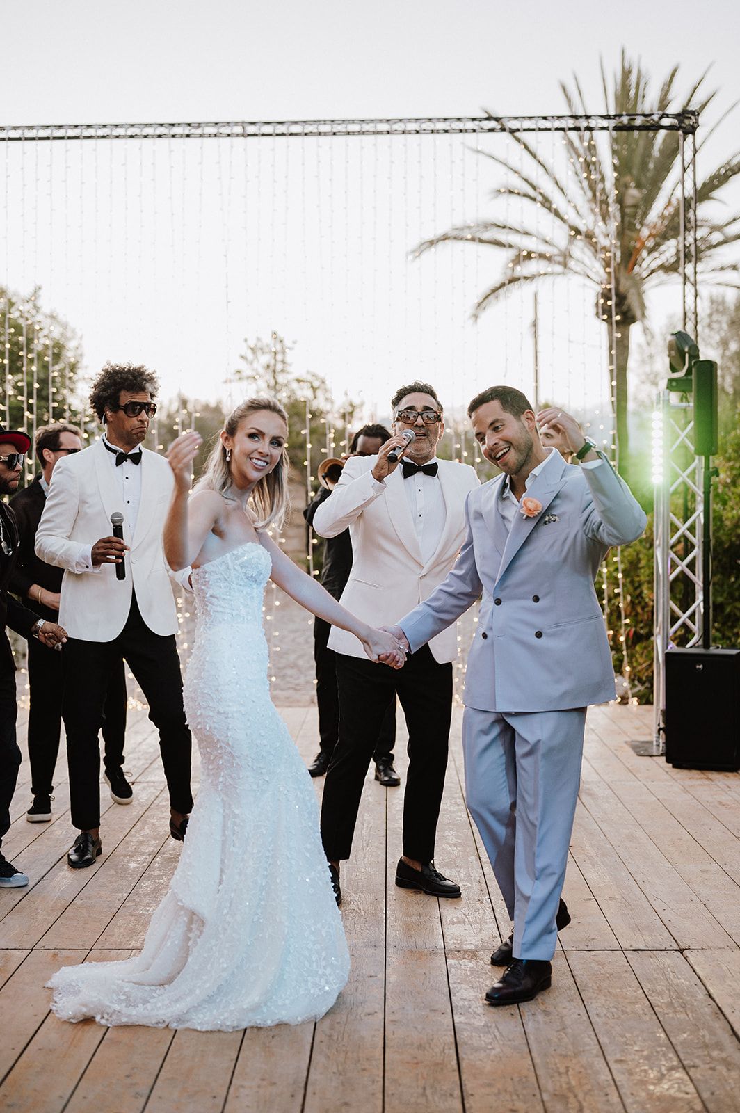 Bride in sequin gown and groom in light blue suit celebrate first dance at outdoor wedding.
