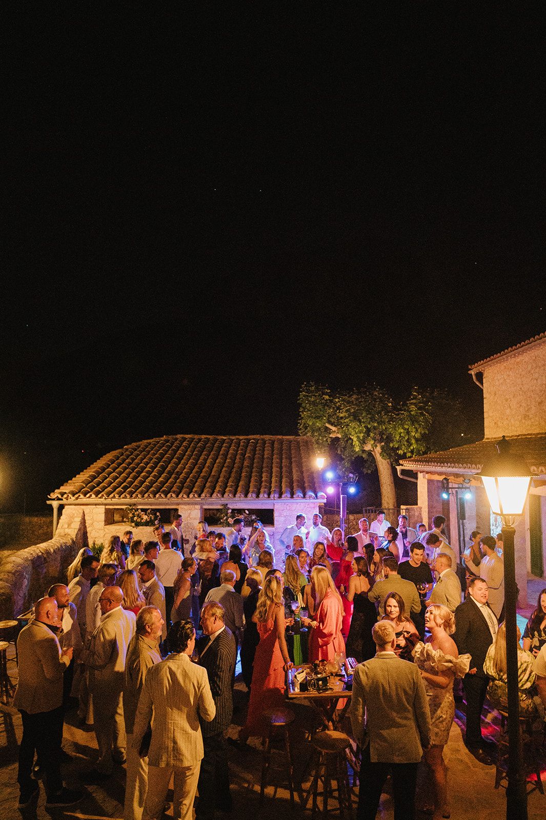 Aerial view of wedding guests mingling at an outdoor nighttime reception venue.