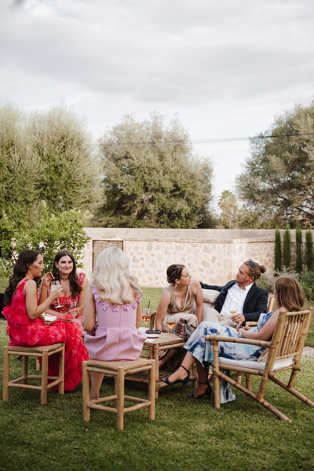 Wedding guests in colorful attire socialize on garden lawn chairs during outdoor cocktail hour reception.