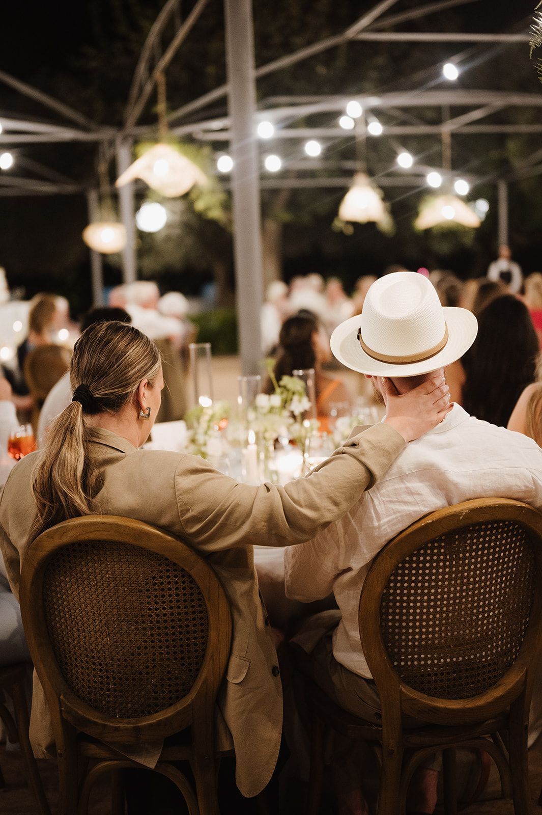 Couple seated at elegant outdoor wedding reception dinner under string lights at night.