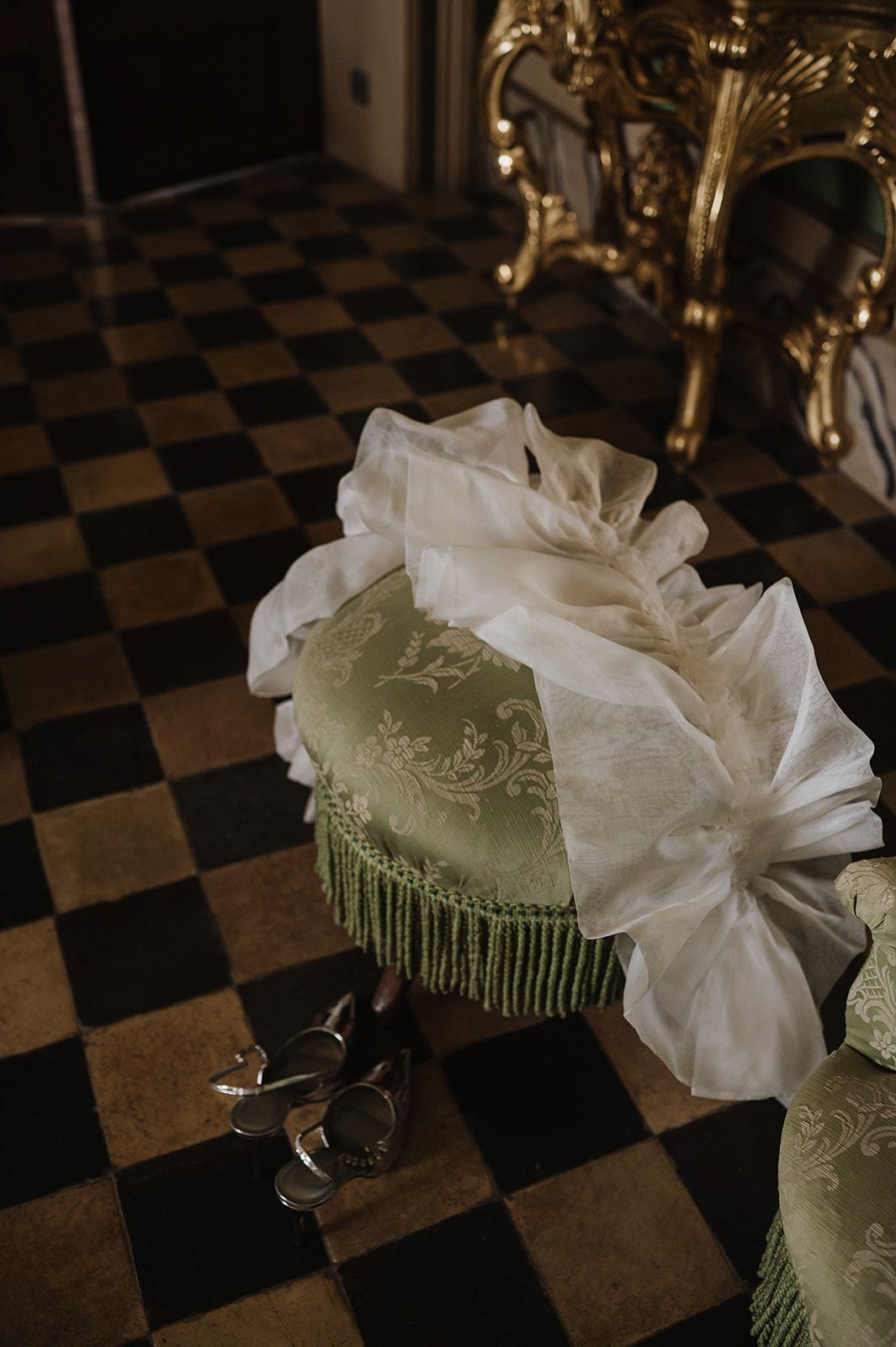 Wedding veil draped over ornate green velvet ottoman on classic checkered floor in elegant venue.