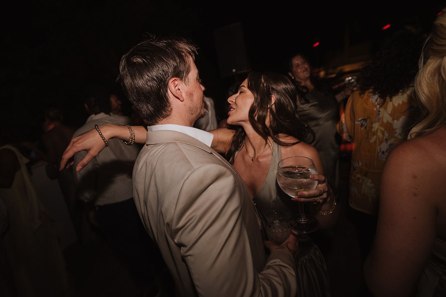 Couple dancing closely together on crowded dance floor at dark romantic wedding reception.