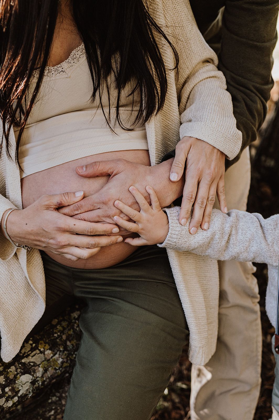 Close-up of family hands lovingly touching pregnant woman's bare baby bump outdoors.
