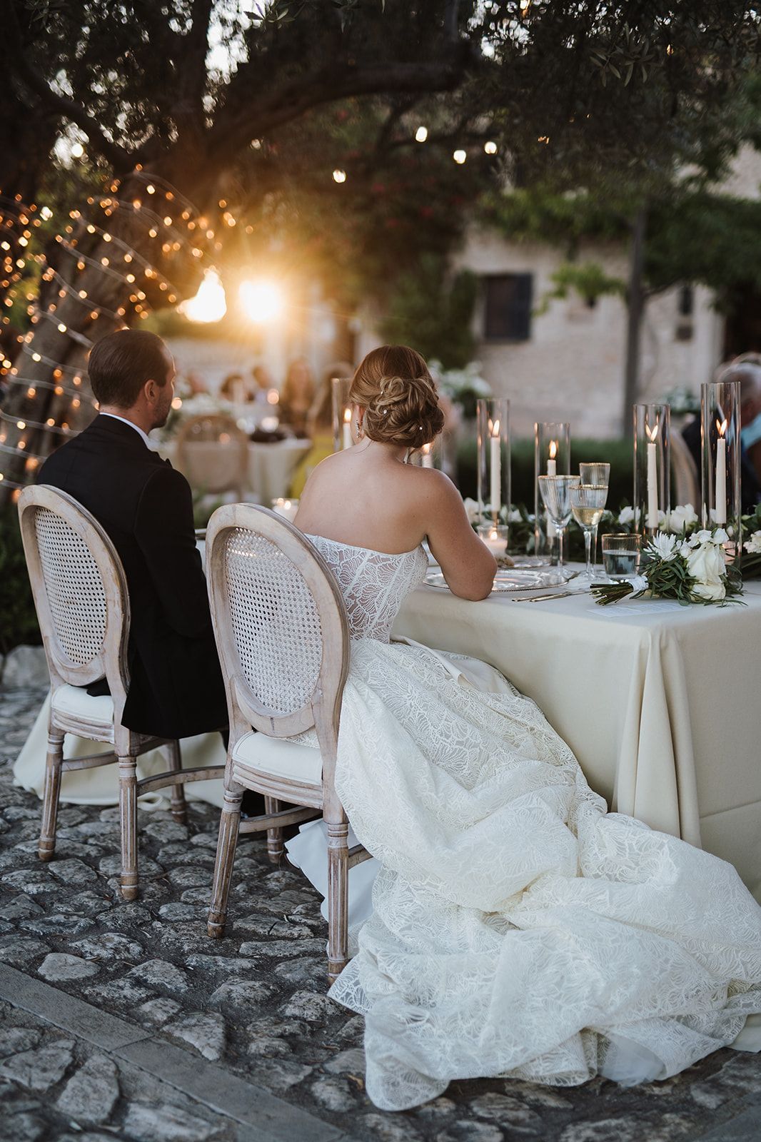 Bride and groom seated at candlelit sweetheart table during outdoor evening reception.