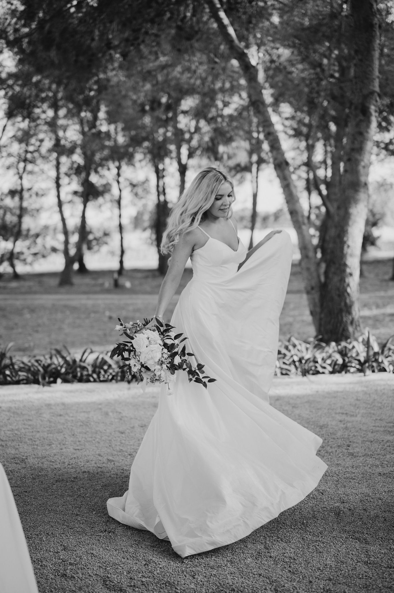 Black and white photo of a bride in a flowing white gown holding a bouquet outdoors.