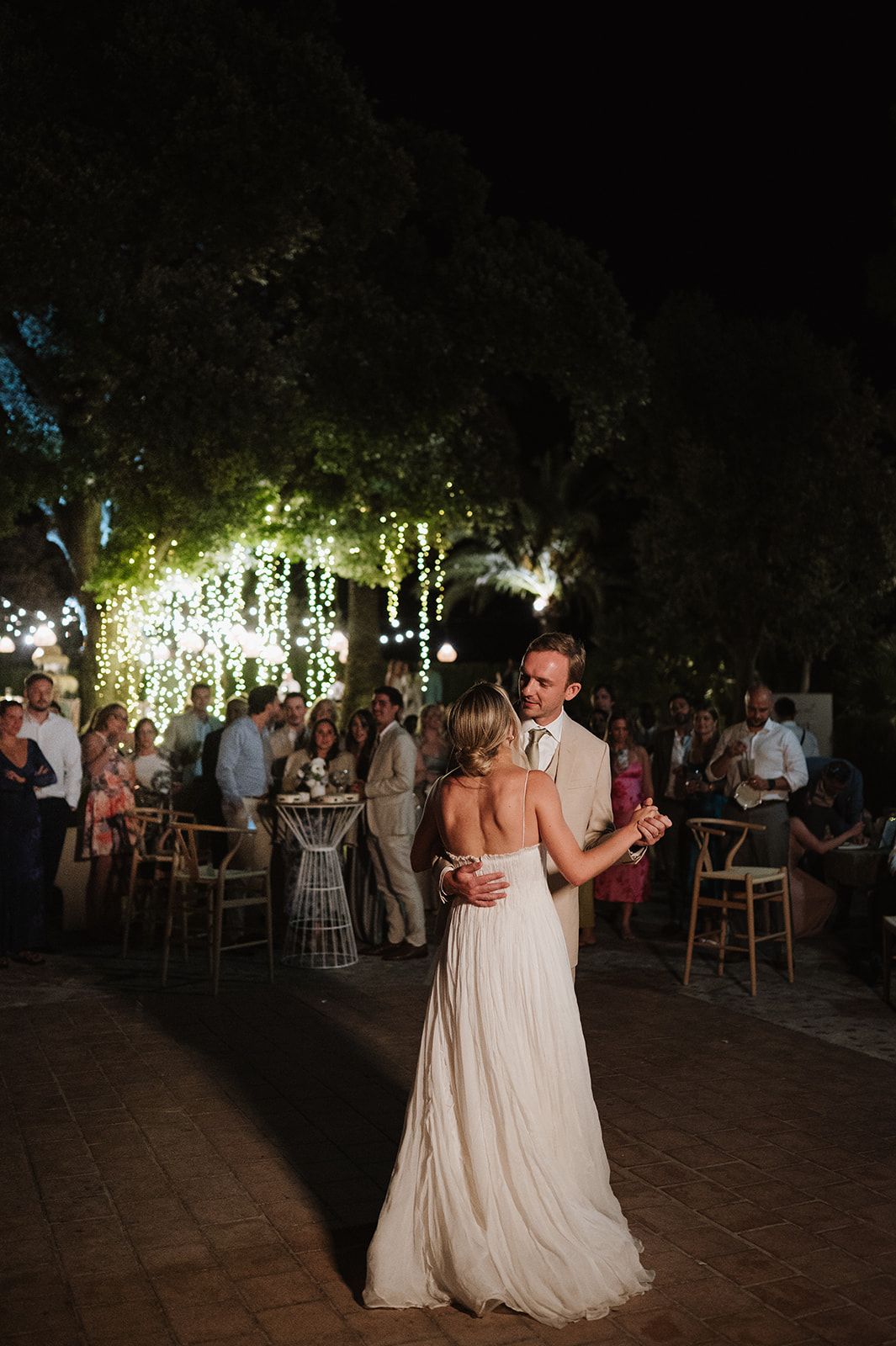 Bride and groom share romantic first dance under sparkling fairy lights at outdoor nighttime wedding reception.