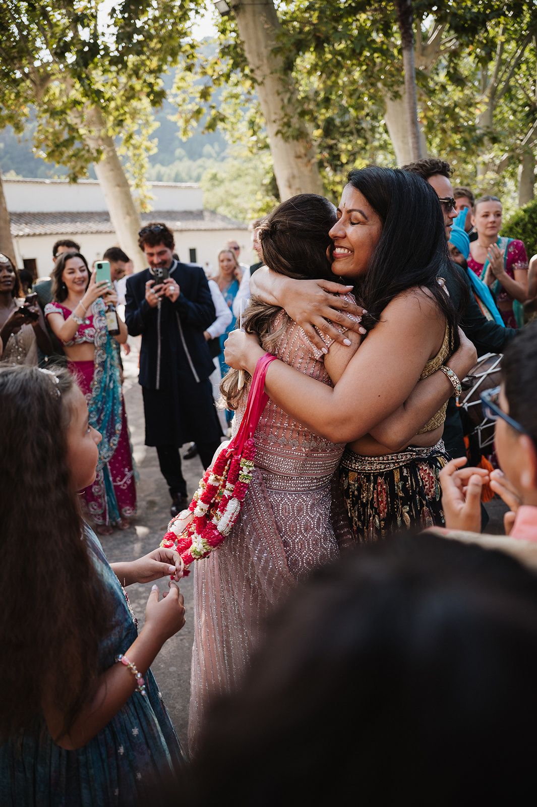 Bride and guest sharing emotional hug during Indian wedding milni ceremony outdoors among guests.