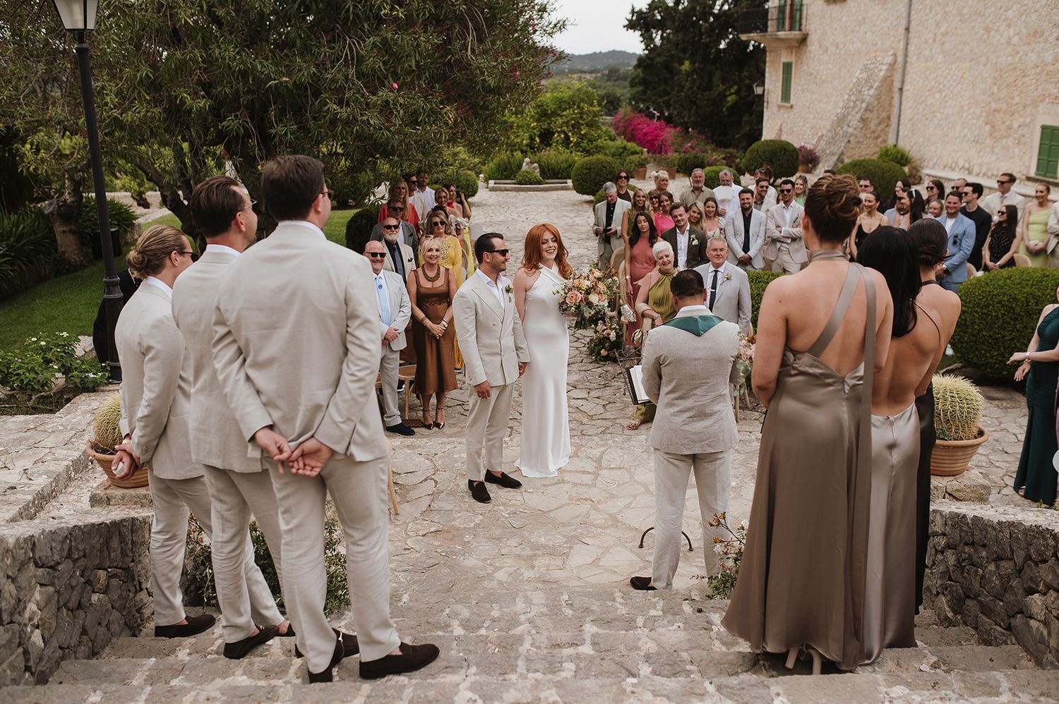 Wedding ceremony gathering with guests surrounding bride and groom at rustic Mediterranean venue.