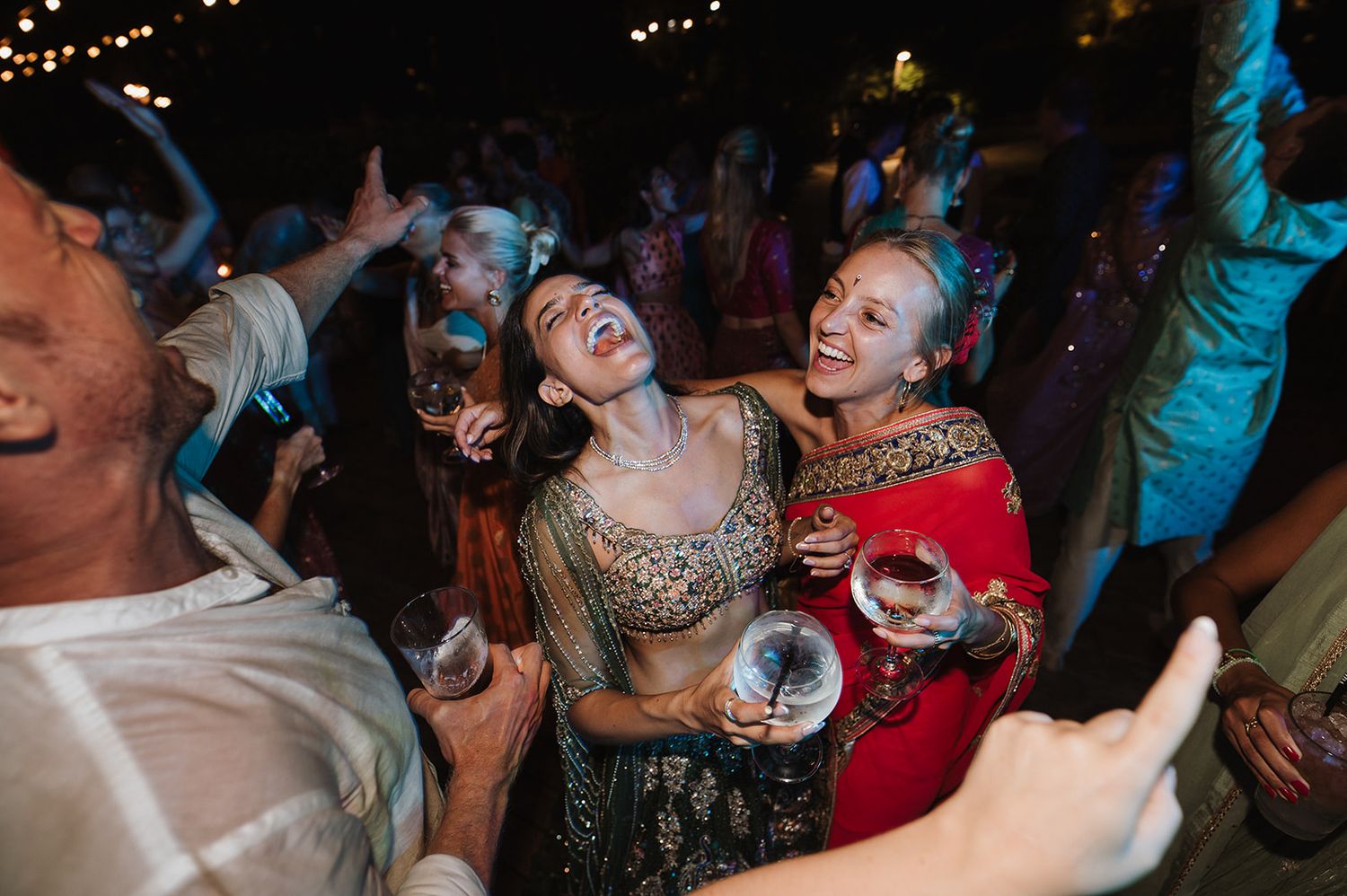 Guests dancing joyfully at vibrant Indian wedding reception party under evening lights.