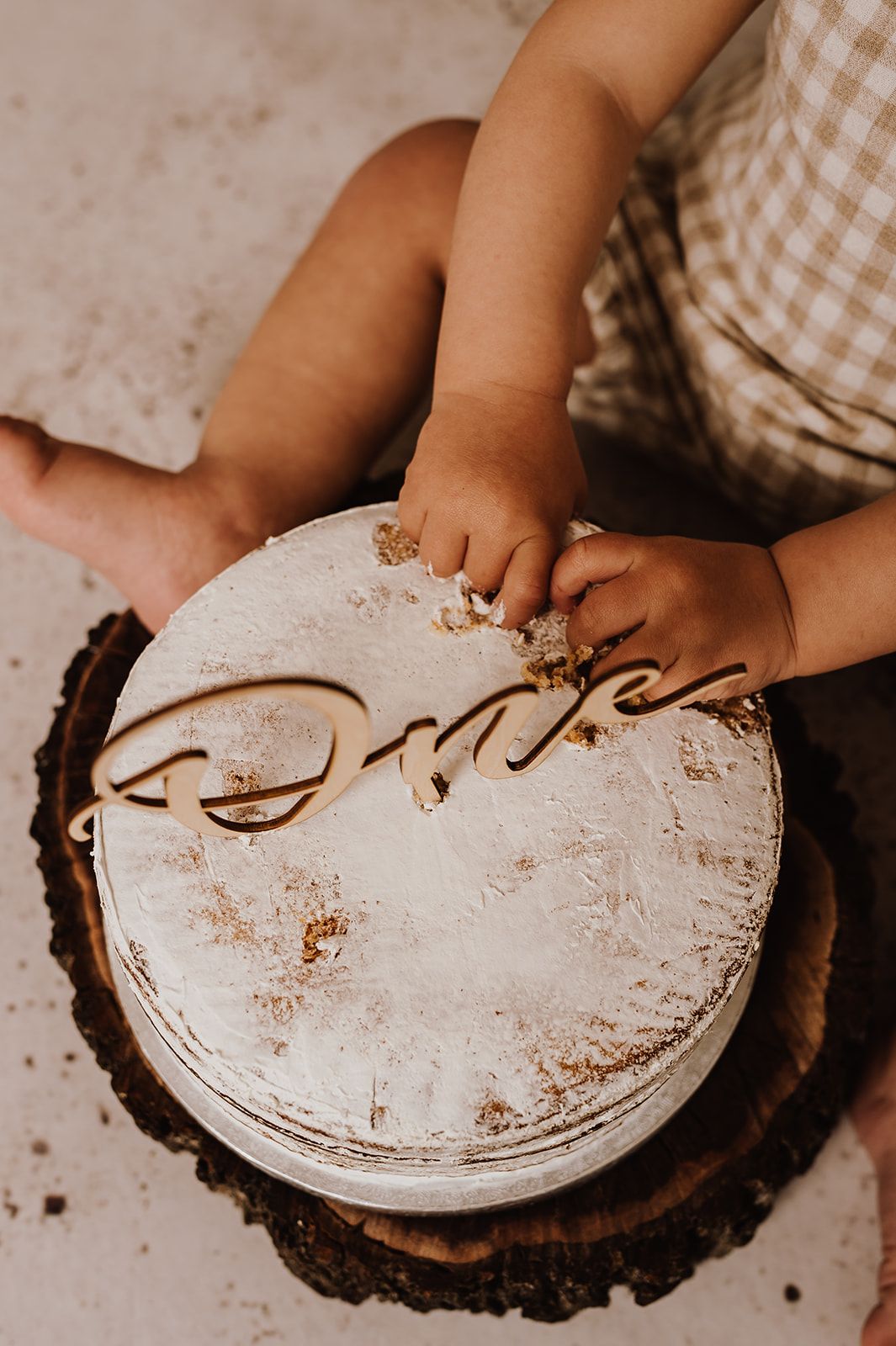 Baby smashing a white frosted cake on a wood slice with a cursive name topper at a first birthday cake smash.