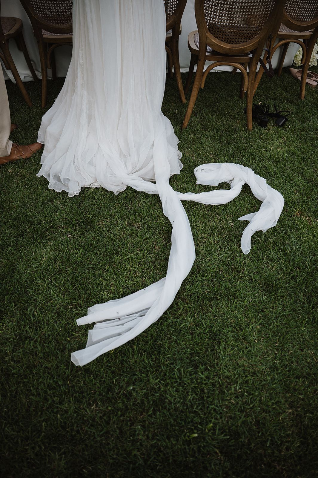 White wedding dress train and ribbon detail resting on lush green grass at outdoor reception.