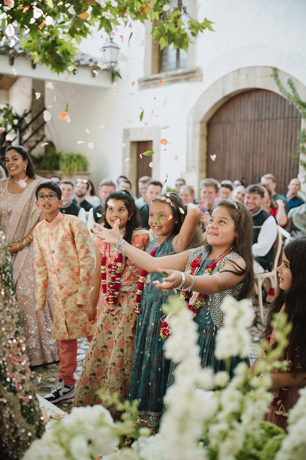 Children in Indian attire tossing flower petals during outdoor Hindu wedding ceremony.