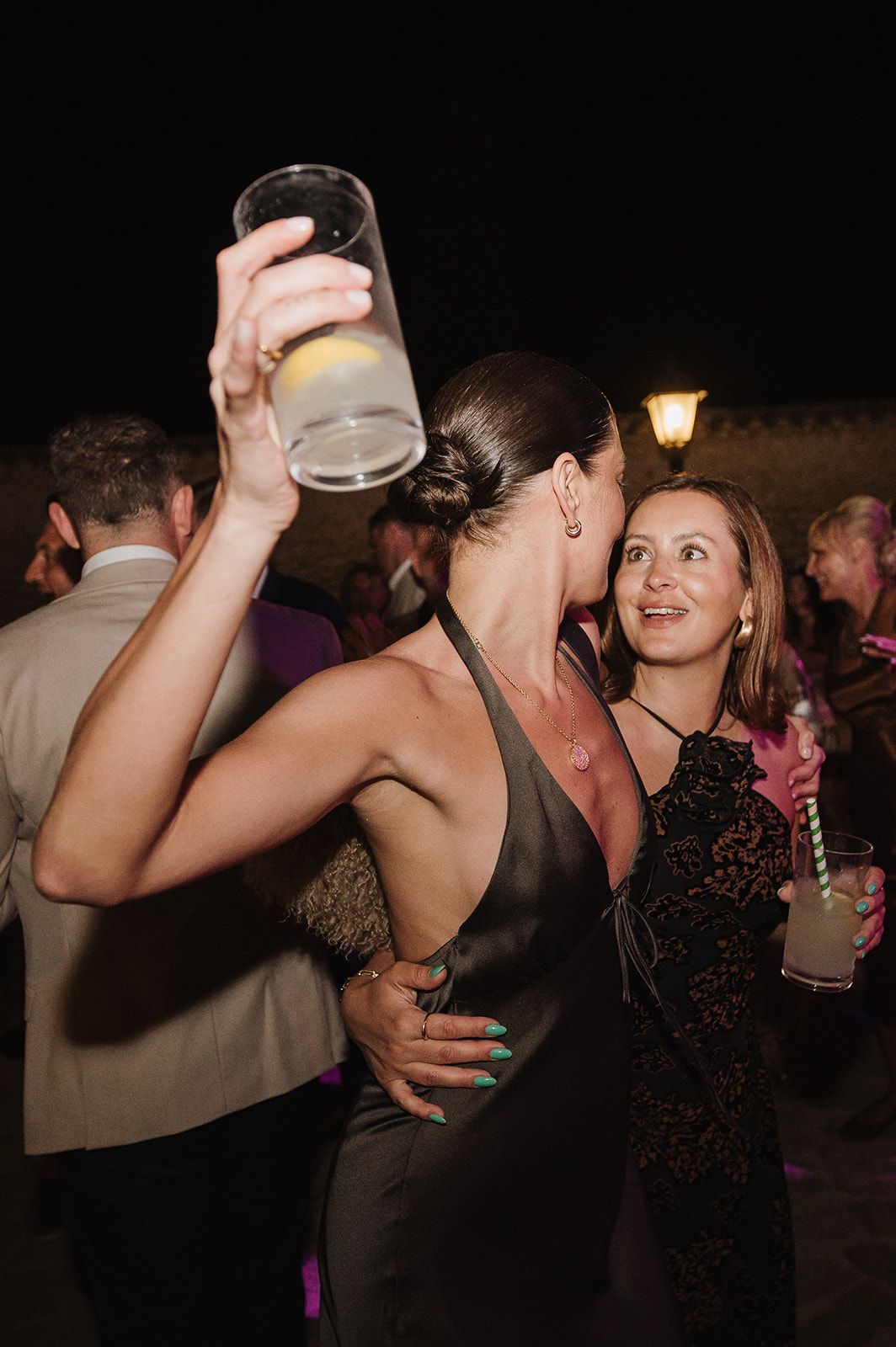 Woman in backless gray dress raising a drink while dancing at an outdoor wedding party.