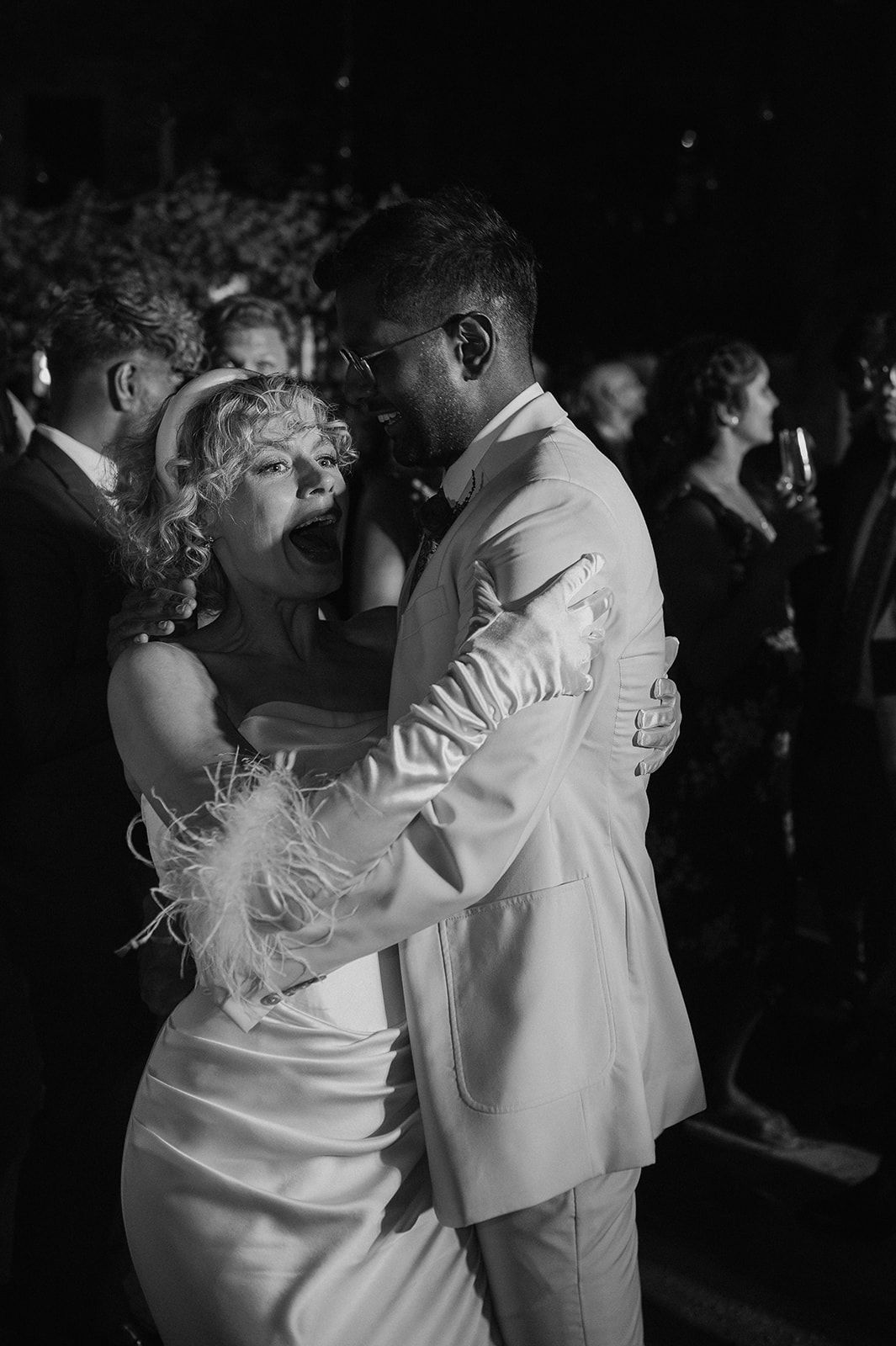 Bride and groom share joyful first dance embrace in black and white wedding reception photo.