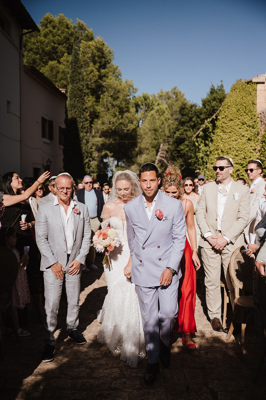 Bride and groom walking through cheering guests after outdoor wedding ceremony in sunny venue.
