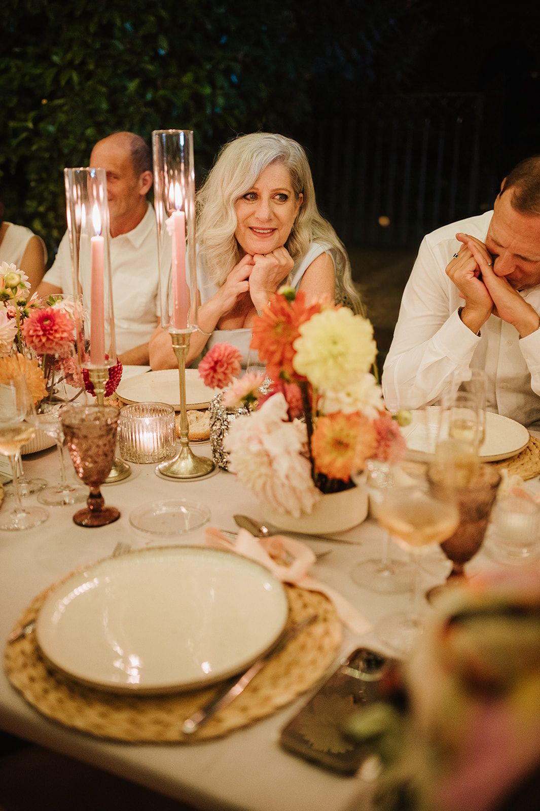 Smiling woman with white hair sits at candlelit wedding reception dinner table.