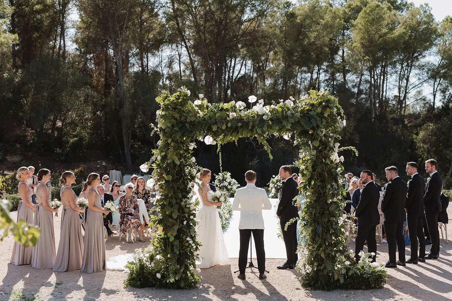 Bride and groom exchange vows beneath a lush floral arch at an outdoor wedding ceremony.