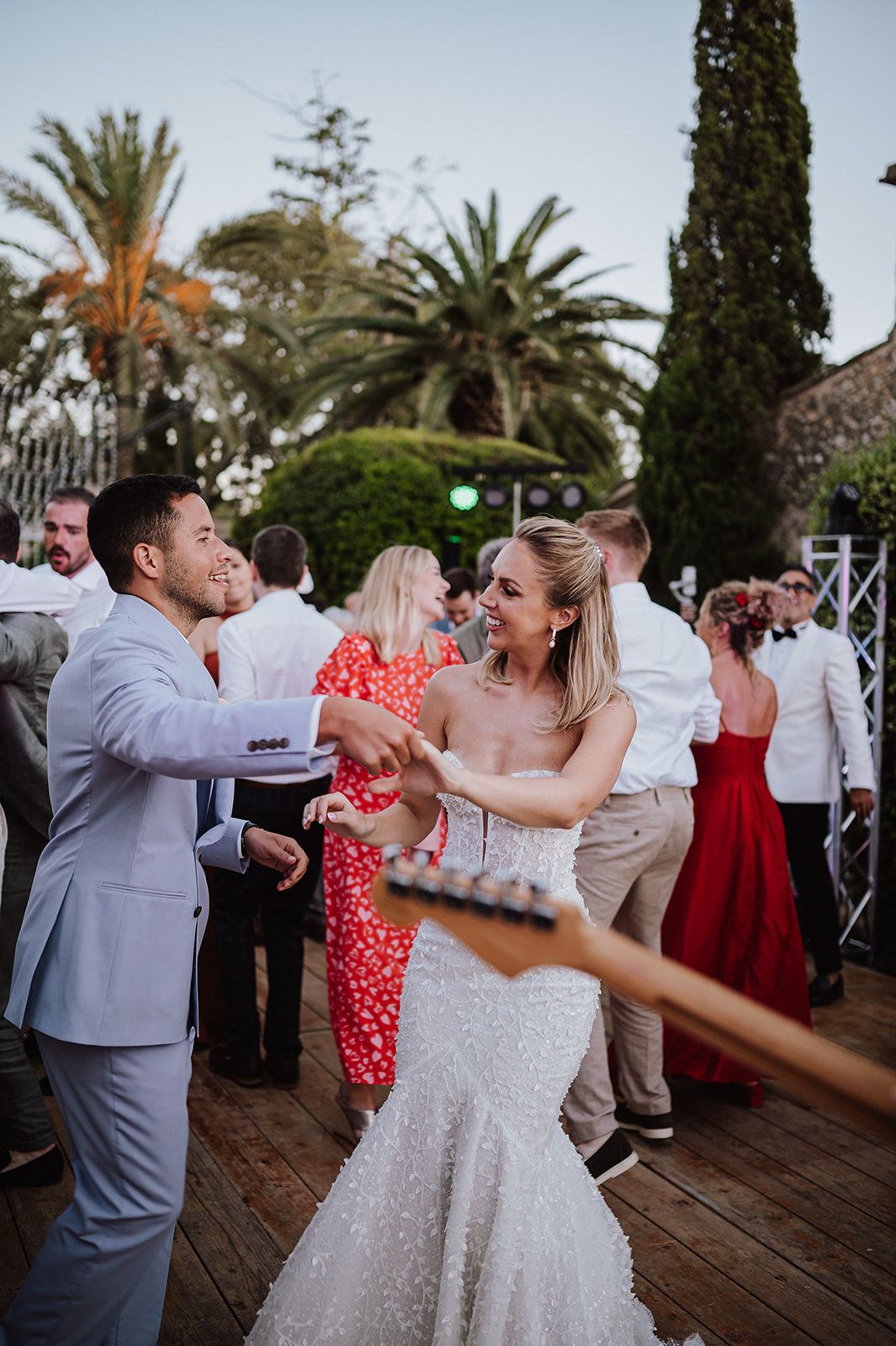 Bride in fitted lace gown dancing joyfully with guest at outdoor wedding reception with palm trees.