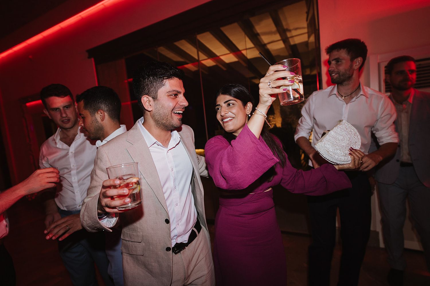 Wedding guests dance and celebrate under red lights at lively indoor wedding after-party.
