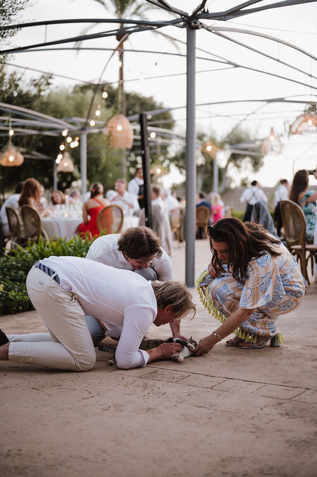 Wedding guests kneeling on patio ground at outdoor evening reception under string lights.
