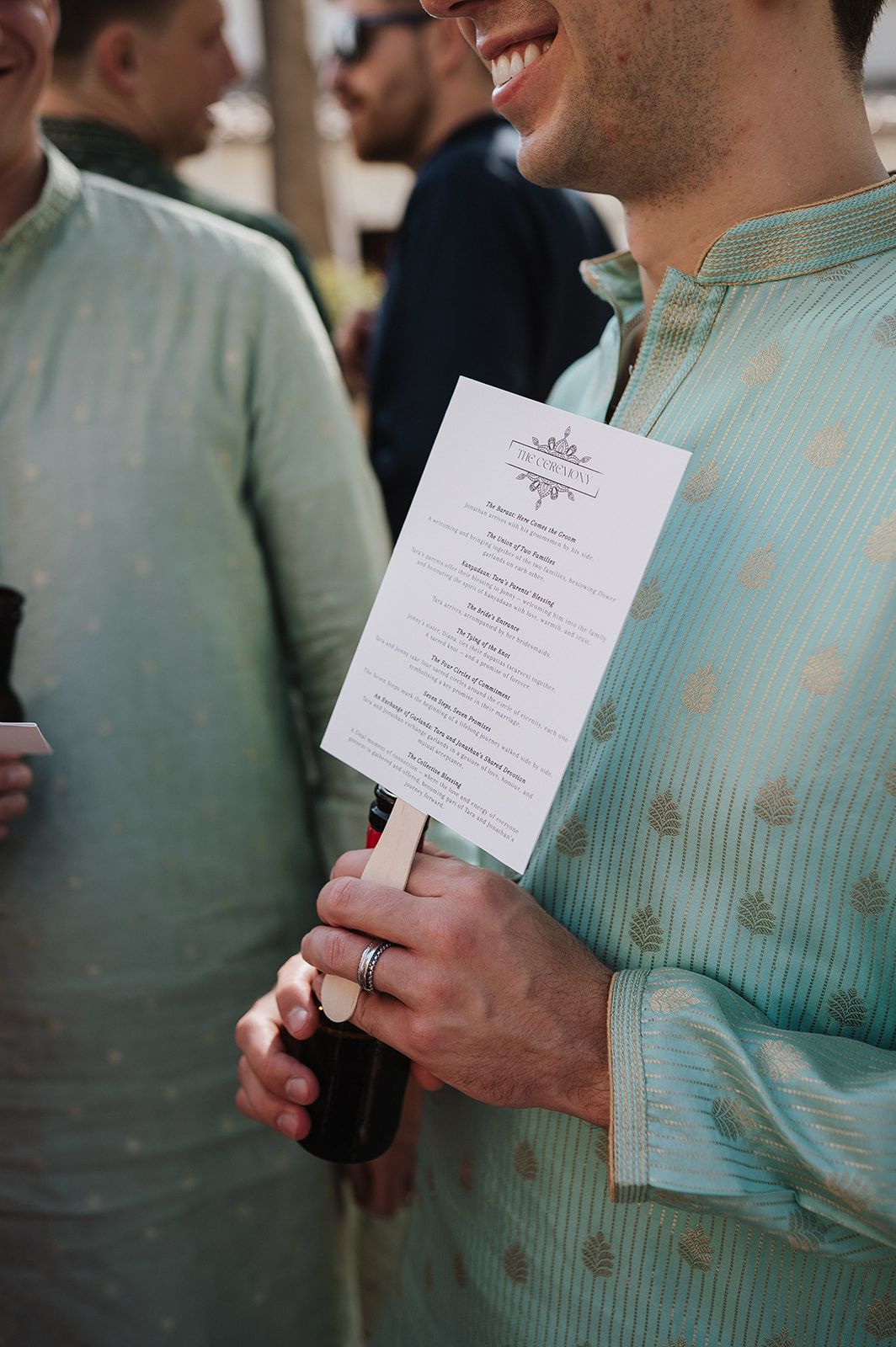 Man in mint green kurta holding a wedding ceremony program at an Indian wedding event.