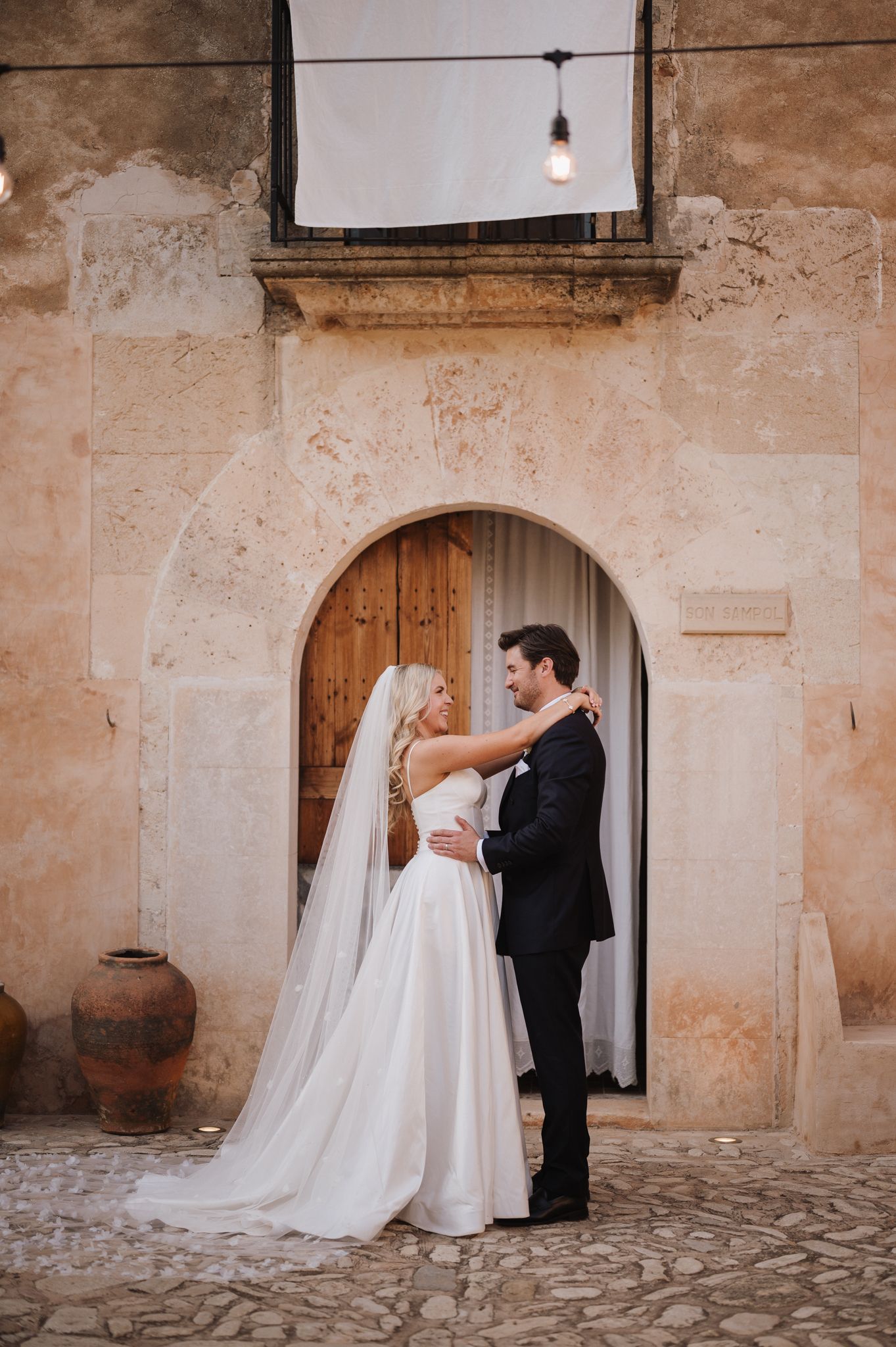 Bride and groom embracing in front of rustic stone archway with wooden door at wedding venue.