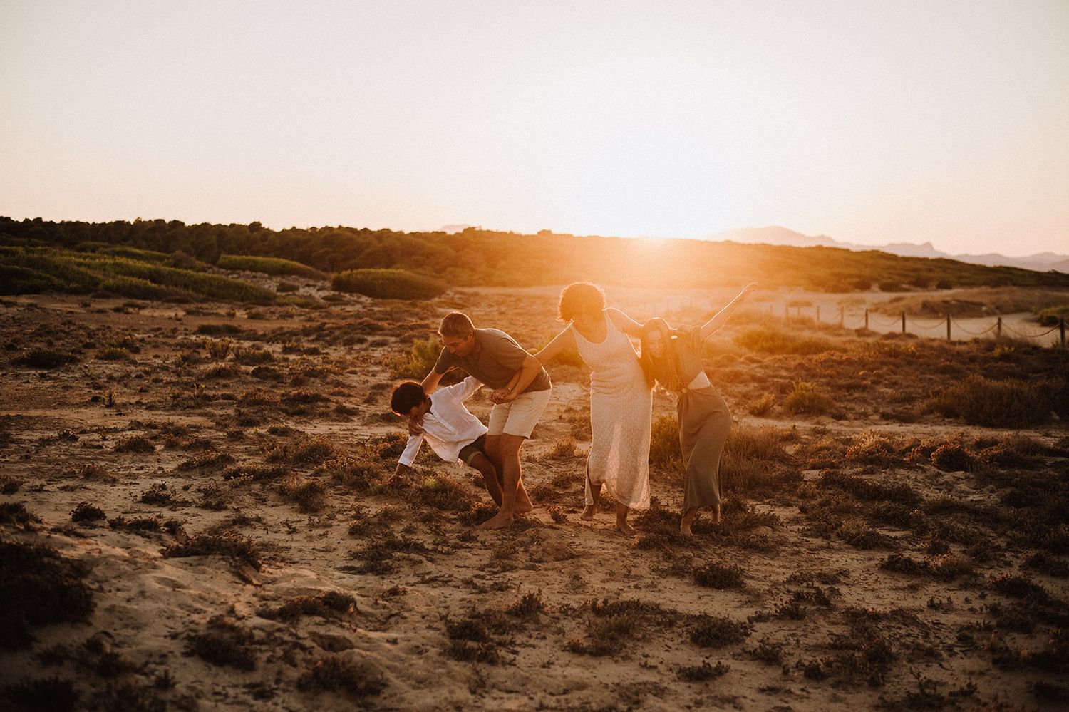 Family with dog playing in sandy dunes during a stunning golden sunset outdoors.