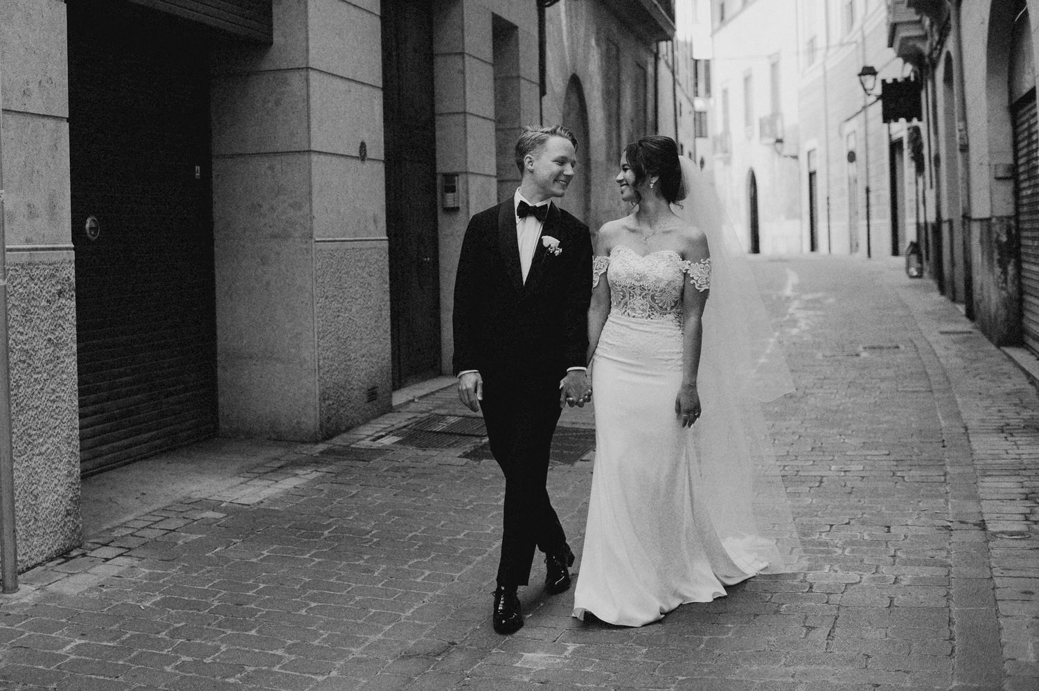 Bride and groom walking together on a cobblestone street in black and white wedding photo.