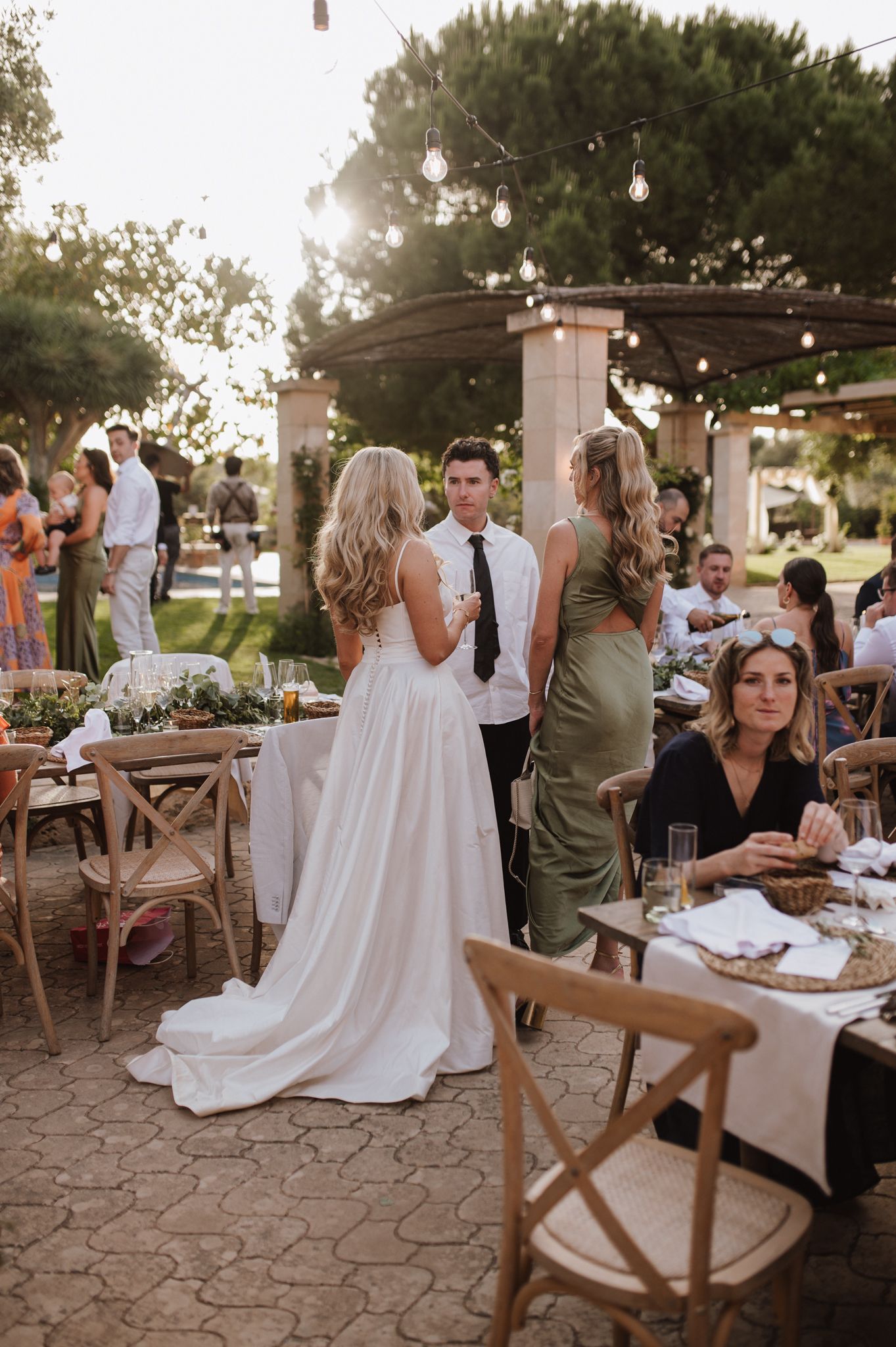 Bride and groom chatting with guests at golden hour outdoor wedding reception.
