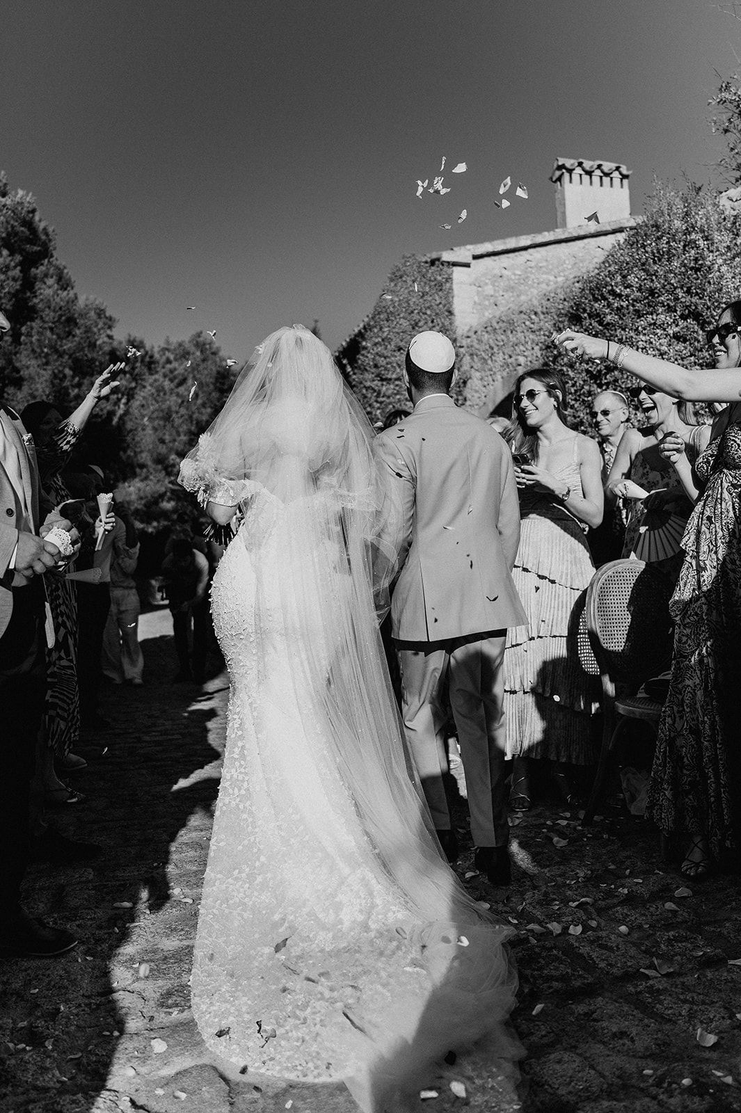 Black and white photo of newlyweds walking through confetti shower after ceremony.