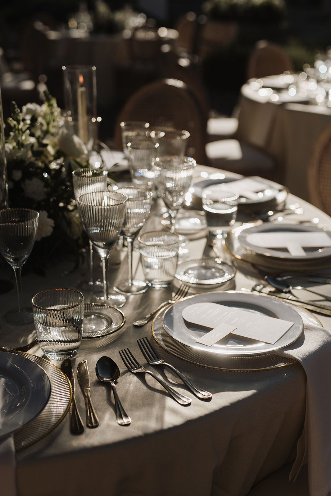 Elegant wedding reception table setting with crystal glassware, gold cutlery, and white floral centerpieces.