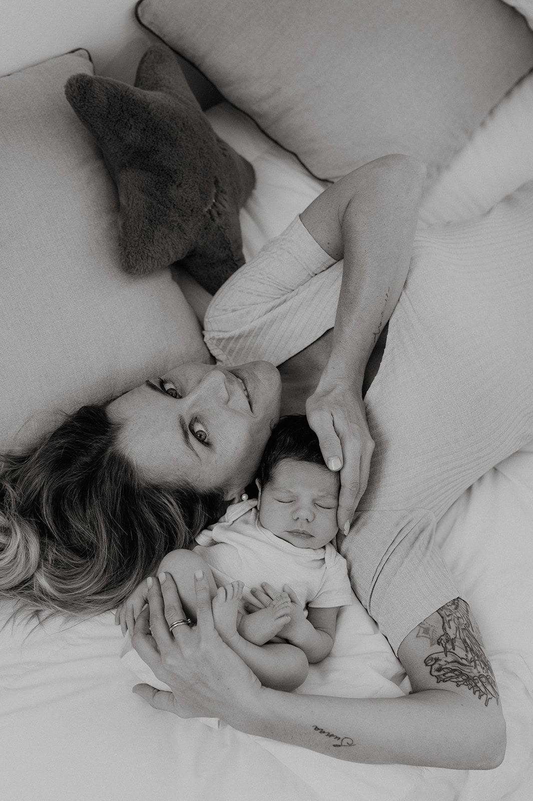 Black and white photo of a mother lying on a bed, tenderly cradling her sleeping newborn baby.
