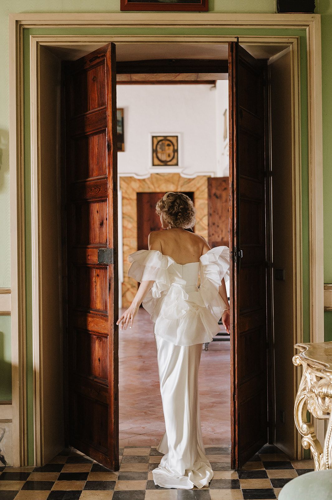 Bride in stunning white structured gown walking through grand wooden doors of luxury wedding venue.