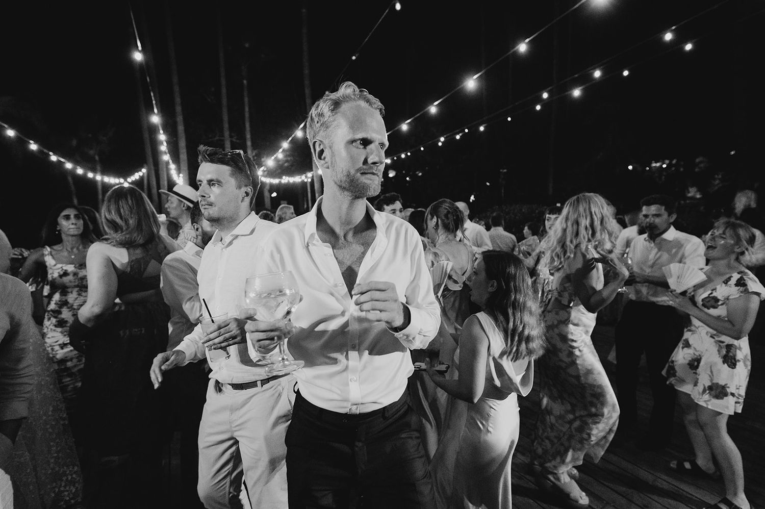 Guests dancing outdoors at a wedding reception under string lights at night.