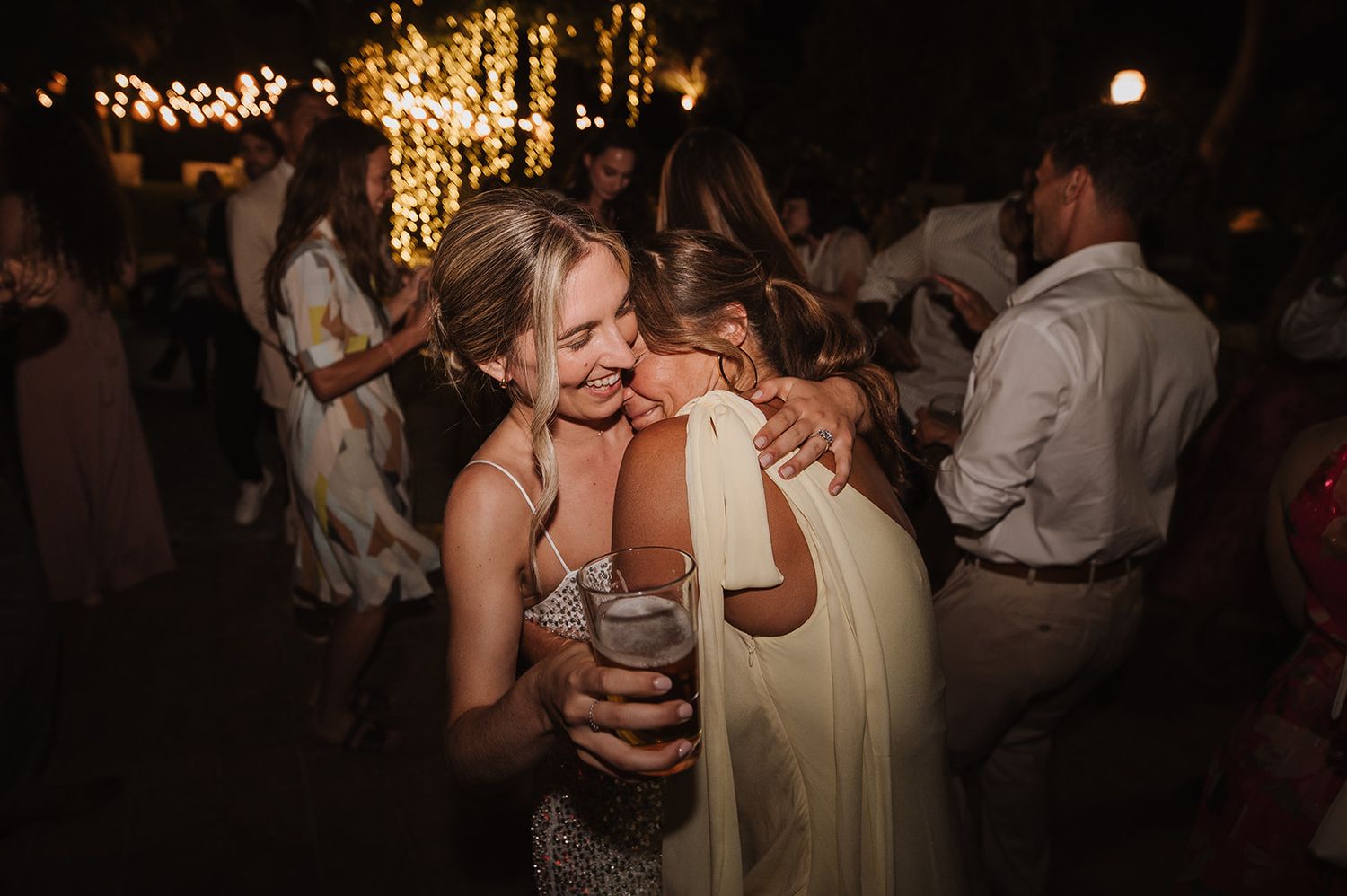Two women sharing a warm embrace while dancing together at an evening outdoor wedding reception.