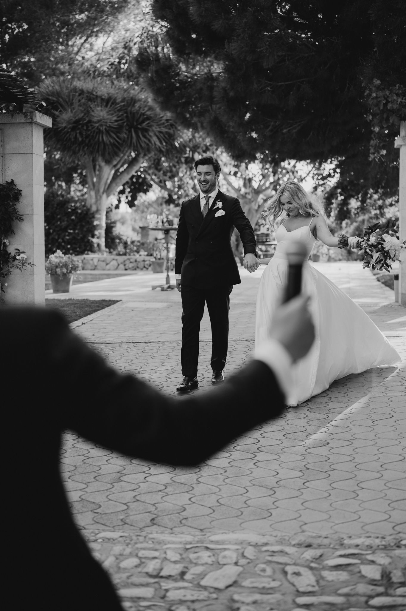 Black and white photo of bride and groom walking path as photographer captures the moment.