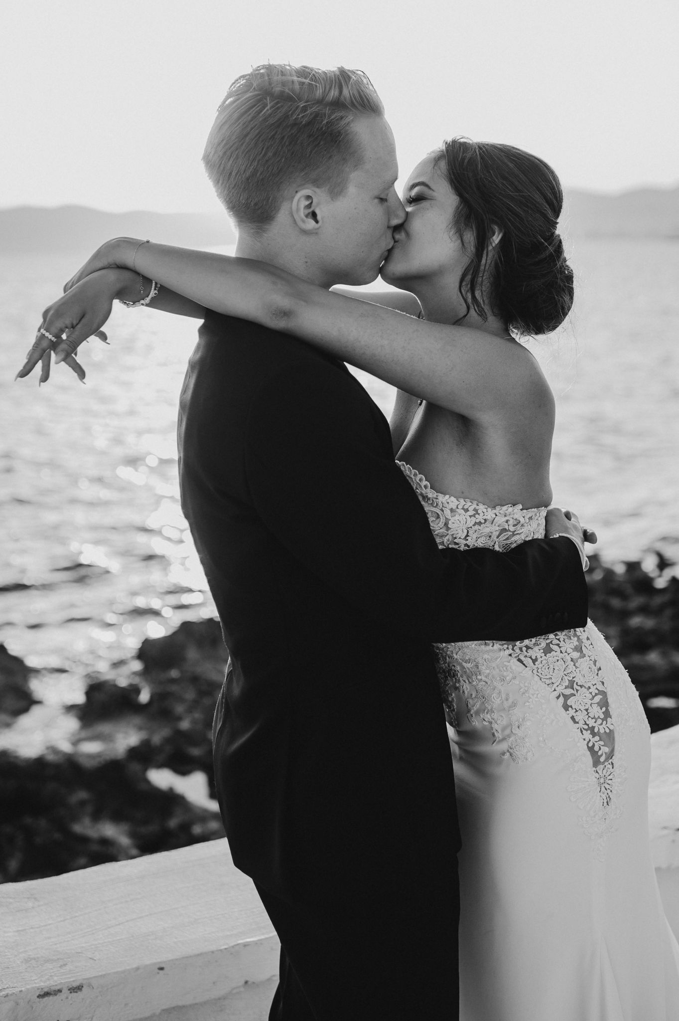 Bride and groom share romantic kiss by the ocean in black and white photo.