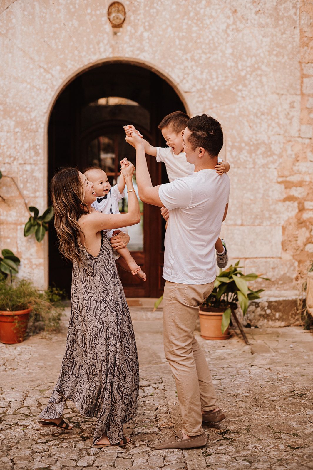 Joyful family of four playing together in a rustic Mediterranean courtyard at golden hour.