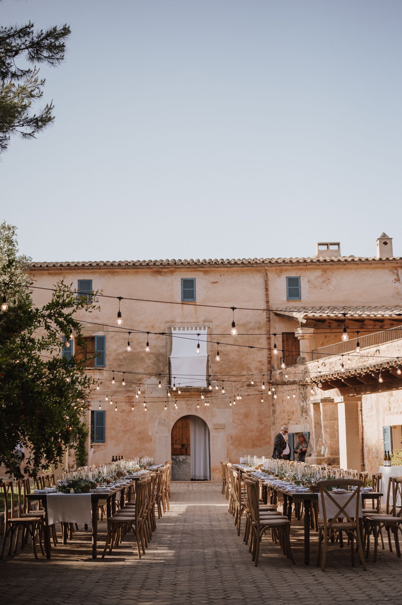 Long reception tables arranged in a courtyard of a rustic Mediterranean estate under string lights.